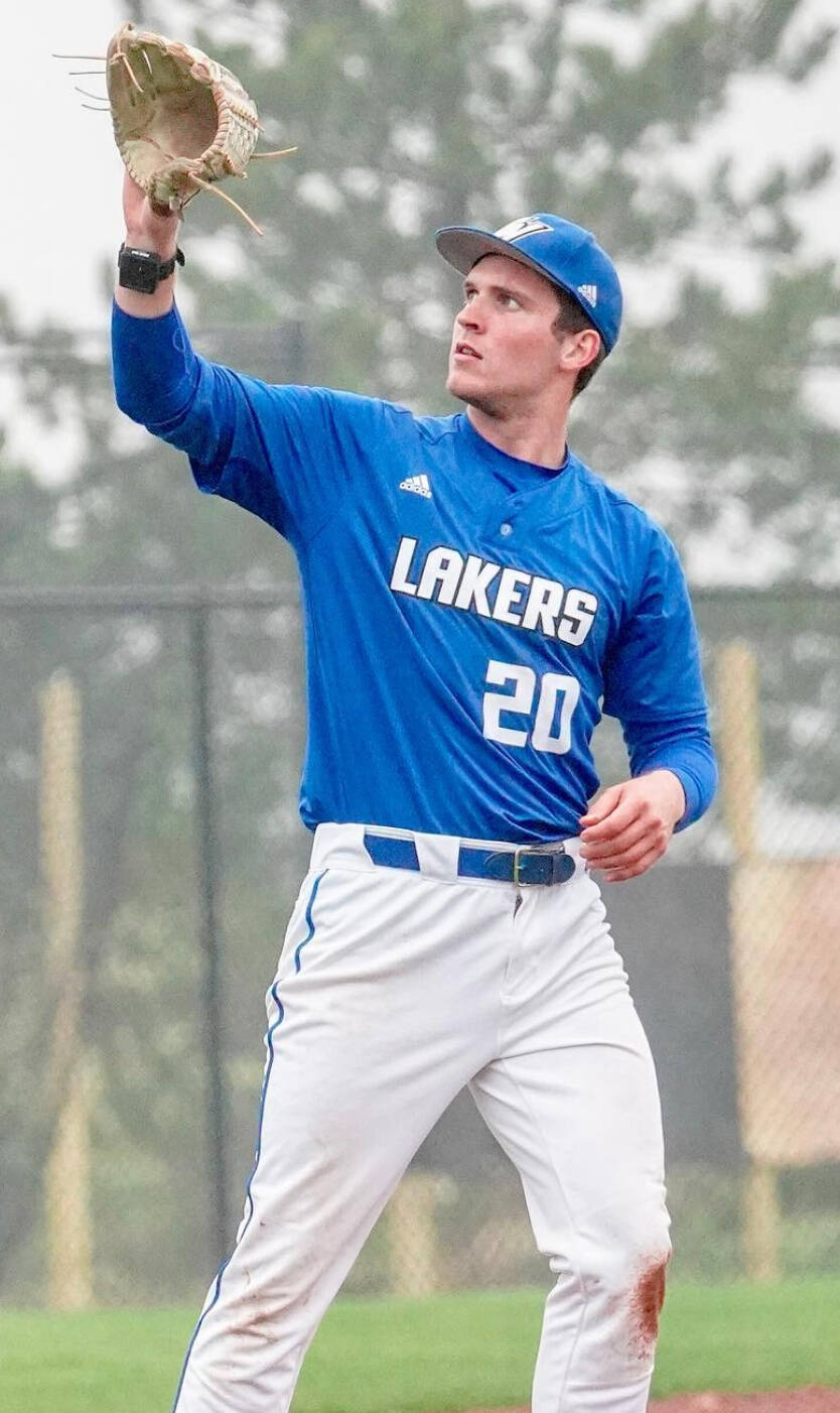 Michael Morawski, a baseball player wearing a blue jersey with 'LAKERS 20' and white pants with blue trim, raising a gloved hand, stands on a field with a chain-link fence and trees in the background.